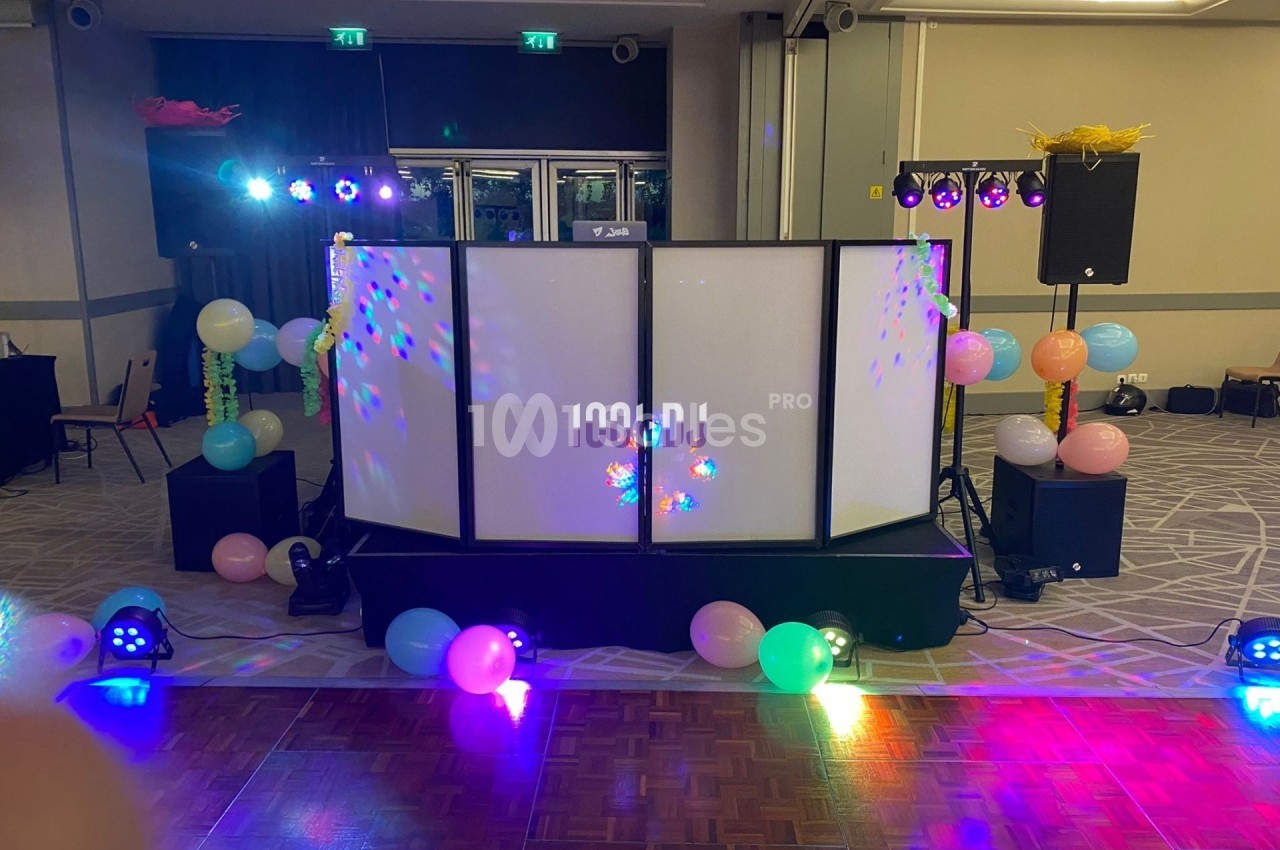 Stand de DJ éclairé avec des jeux de lumières colorés, entouré de ballons dans une salle de réception.