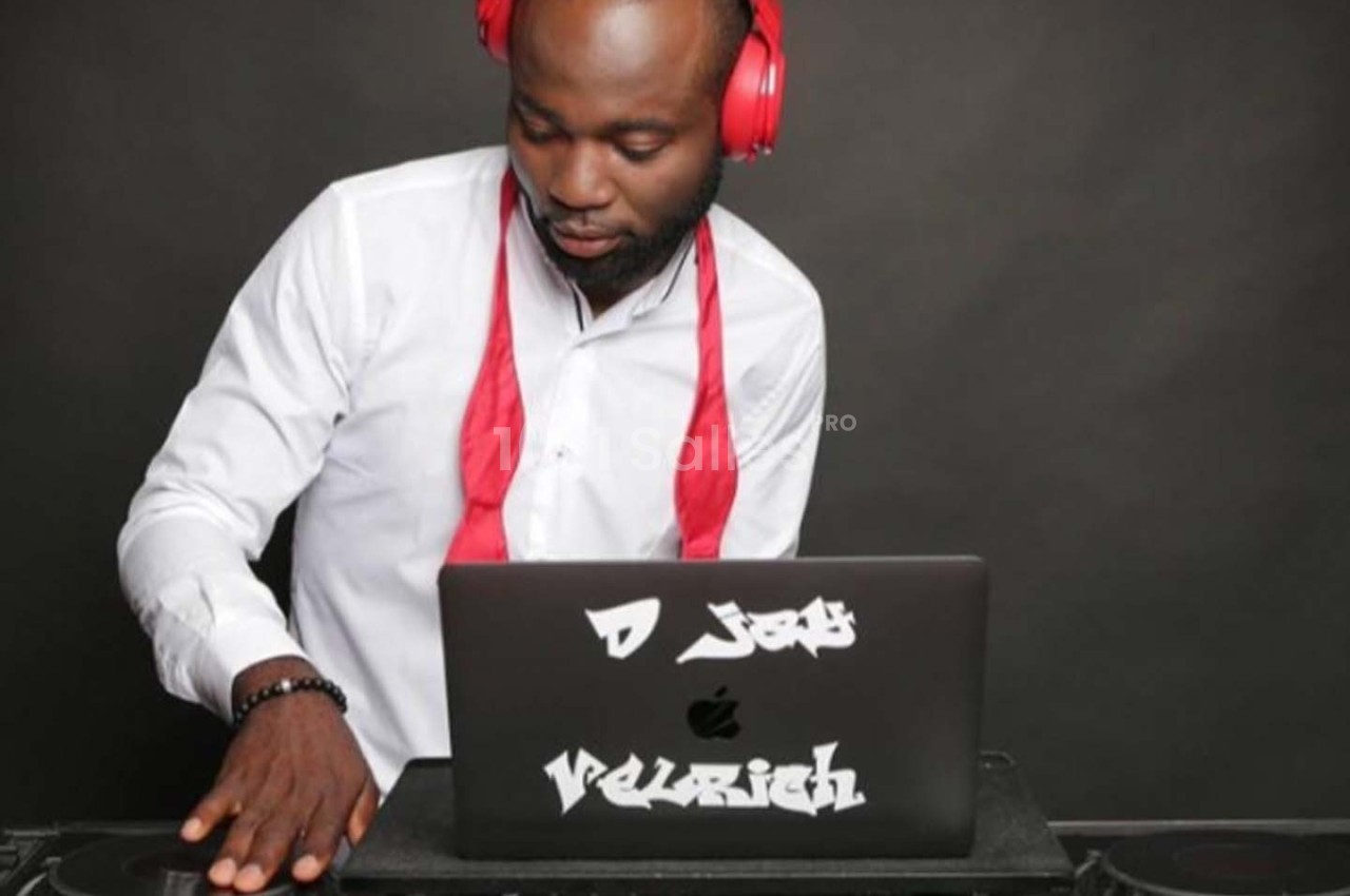 Un DJ portant un casque rouge mixe de la musique sur un ordinateur portable avec un fond sombre.