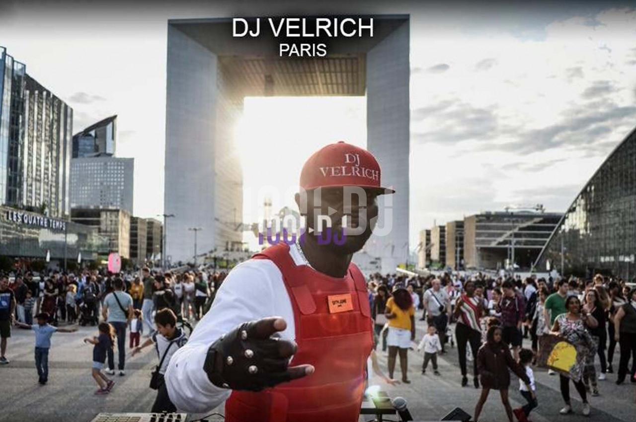 Un DJ mixant en plein air devant une foule, avec l'Arche de la Défense en arrière-plan au coucher du soleil.