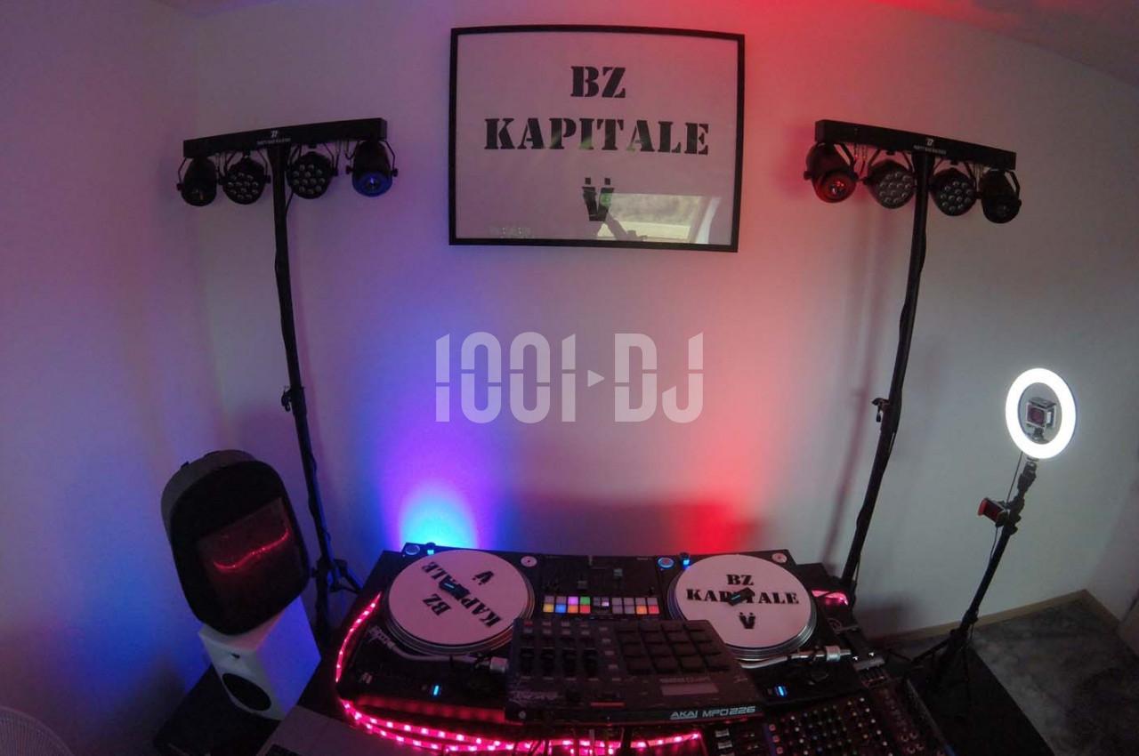 Poste de DJ avec platines, table de mixage, éclairages colorés et panneau ’BZ KAPITALE’ sur le mur.