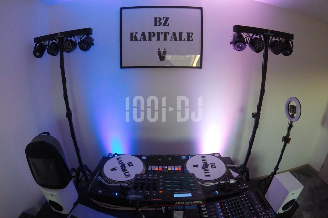 Deux platines, une table de mixage et des éclairages installés dans une pièce avec un cadre ’BZ KAPITALE’ au mur.