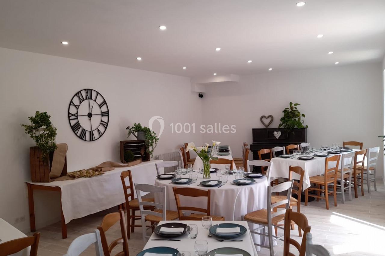 Salle lumineuse aménagée pour un repas, avec tables rondes dressées, chaises en bois et décoration végétale.