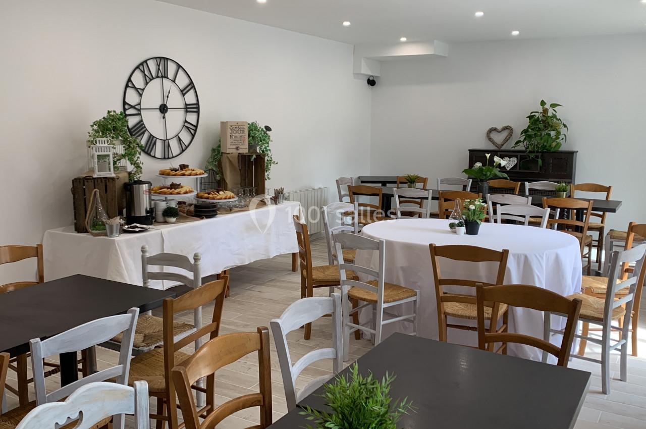 Salle lumineuse aménagée avec des tables et chaises en bois, buffet décoré de plantes et horloge murale.