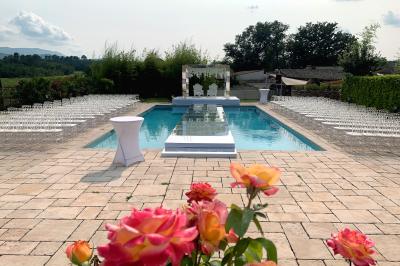 Allée centrale bordée de chaises blanches menant à une arche décorée de fleurs, dans un cadre extérieur arboré.
