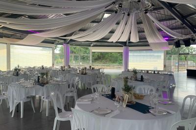 Allée centrale bordée de chaises blanches menant à une arche décorée de fleurs, dans un cadre extérieur arboré.