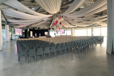 Allée centrale bordée de chaises blanches menant à une arche décorée de fleurs, dans un cadre extérieur arboré.