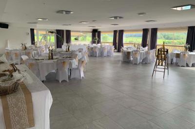 Allée centrale bordée de chaises blanches menant à une arche décorée de fleurs, dans un cadre extérieur arboré.