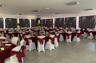 Allée centrale bordée de chaises blanches menant à une arche décorée de fleurs, dans un cadre extérieur arboré.