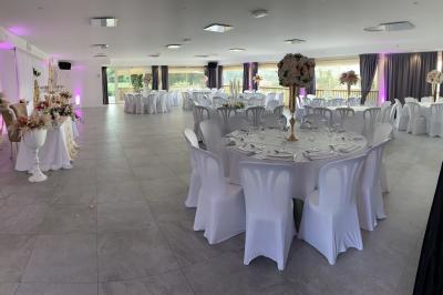 Allée centrale bordée de chaises blanches menant à une arche décorée de fleurs, dans un cadre extérieur arboré.