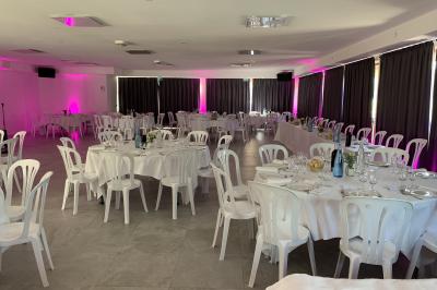 Allée centrale bordée de chaises blanches menant à une arche décorée de fleurs, dans un cadre extérieur arboré.