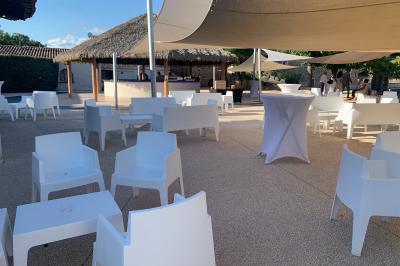 Allée centrale bordée de chaises blanches menant à une arche décorée de fleurs, dans un cadre extérieur arboré.