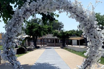 Allée centrale bordée de chaises blanches menant à une arche décorée de fleurs, dans un cadre extérieur arboré.