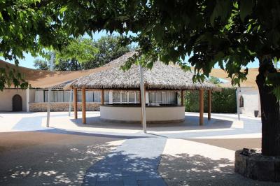 Allée centrale bordée de chaises blanches menant à une arche décorée de fleurs, dans un cadre extérieur arboré.