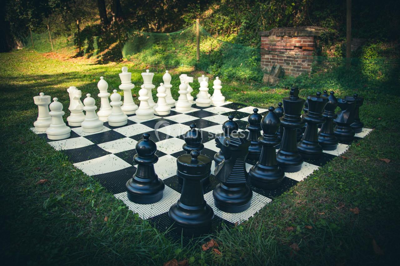 Échiquier géant en plein air avec des pièces blanches et noires disposées pour une partie.
