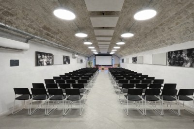 Couloir voûté éclairé par des lumières colorées, avec des murs usés et des fenêtres sur un côté.