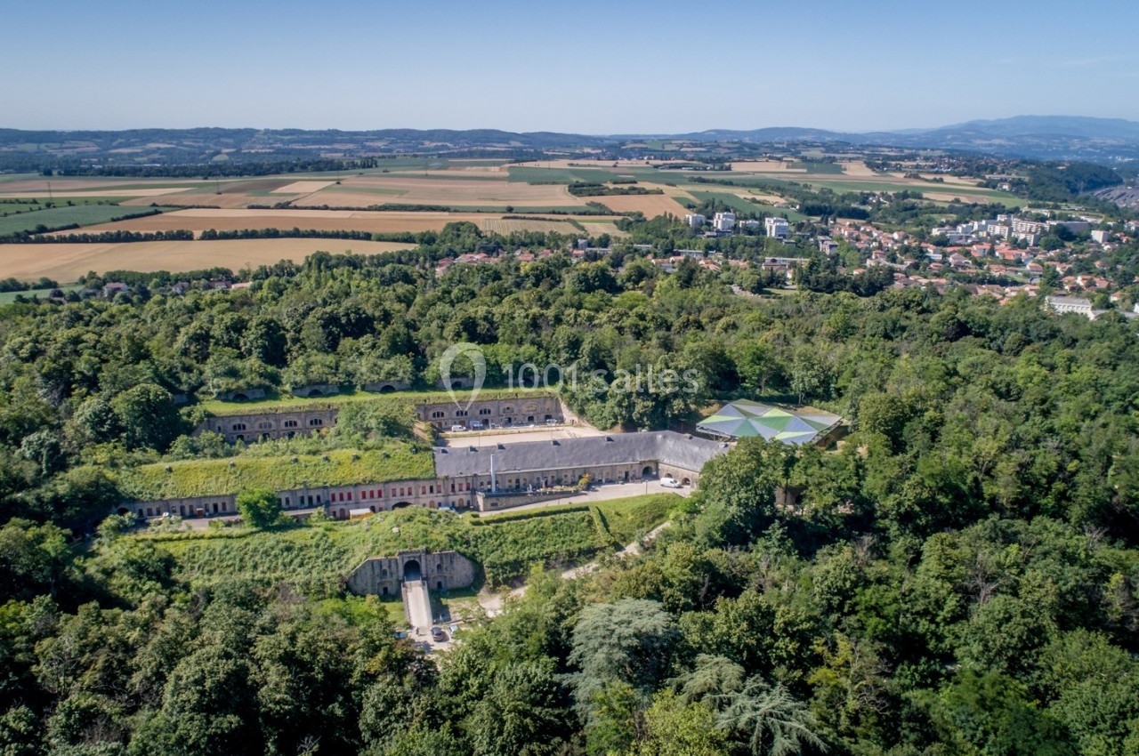 Vue aérienne d'un fort entouré de végétation, avec des champs et une ville en arrière-plan.