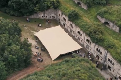 Serveur portant un plateau dans un événement en plein air sous des tentes, avec des invités assis et debout.