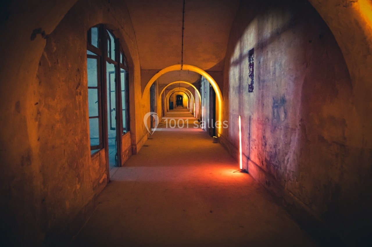 Couloir ancien avec arches éclairé par des lumières colorées, créant une ambiance chaleureuse et mystérieuse.