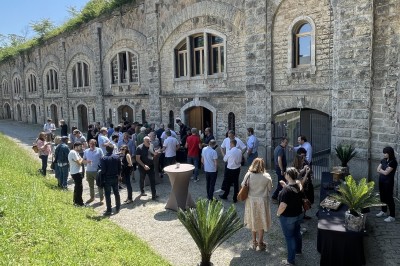 Serveur portant un plateau dans un événement en plein air sous des tentes, avec des invités assis et debout.