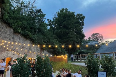 Serveur portant un plateau dans un événement en plein air sous des tentes, avec des invités assis et debout.