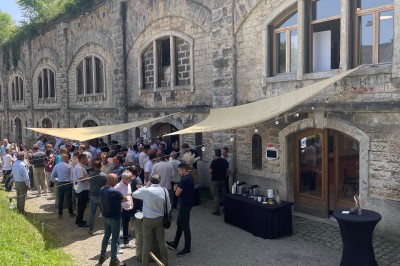 Serveur portant un plateau dans un événement en plein air sous des tentes, avec des invités assis et debout.