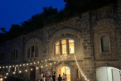 Serveur portant un plateau dans un événement en plein air sous des tentes, avec des invités assis et debout.