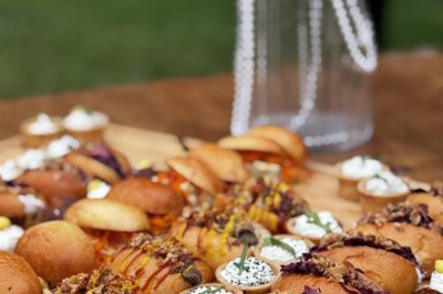 Serveur portant un plateau dans un événement en plein air sous des tentes, avec des invités assis et debout.