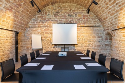 Miniature Fort de Vaise Salle de réunion en pierre avec table rectangulaire, chaises noires, rétroprojecteur, écran blanc et tableau de conférence.