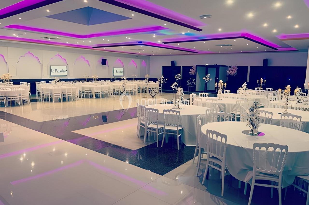 Salle de réception élégante avec tables rondes dressées, éclairage violet et décoration raffinée.
