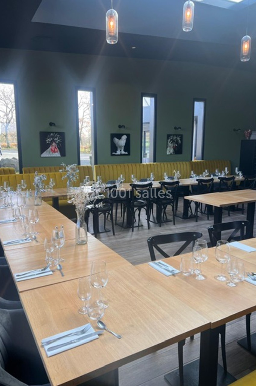 Salle de restaurant lumineuse avec de grandes tables en bois dressées, chaises noires et banquettes jaunes.