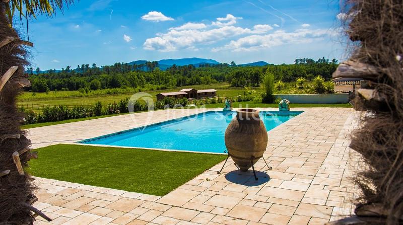 Piscine extérieure entourée de pavés, pelouse artificielle et paysage rural avec collines en arrière-plan.