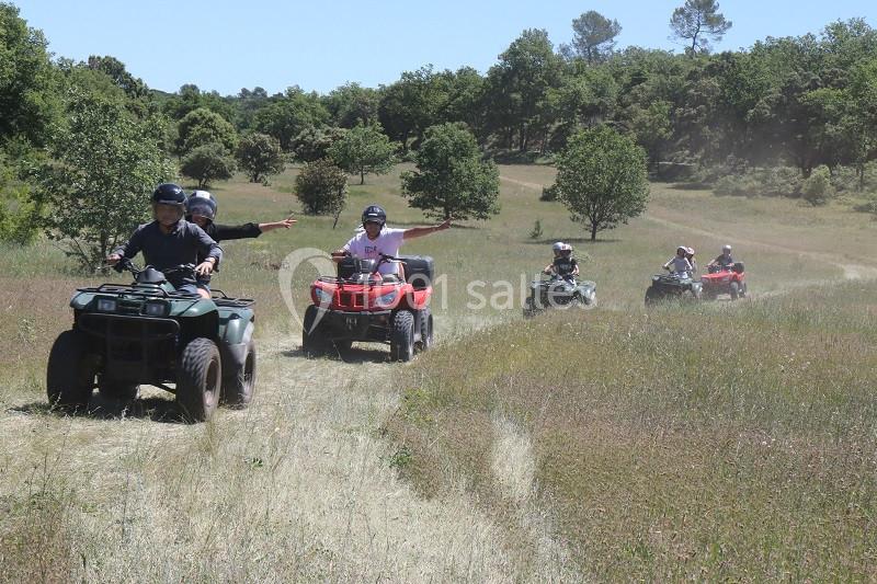 Des personnes conduisent des quads sur un chemin herbeux entouré de végétation et d'arbres.