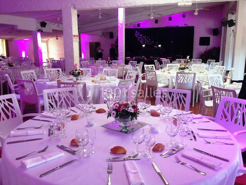 Salle de réception décorée avec des tables rondes dressées, nappes blanches, fleurs et éclairage tamisé.