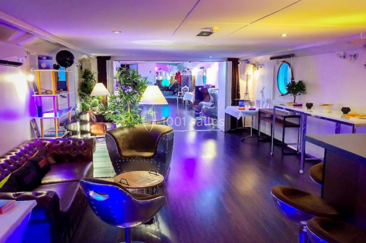 Espace intérieur lumineux avec fauteuils, tables, plantes et éclairage coloré, aménagé dans un style moderne et chaleureux.