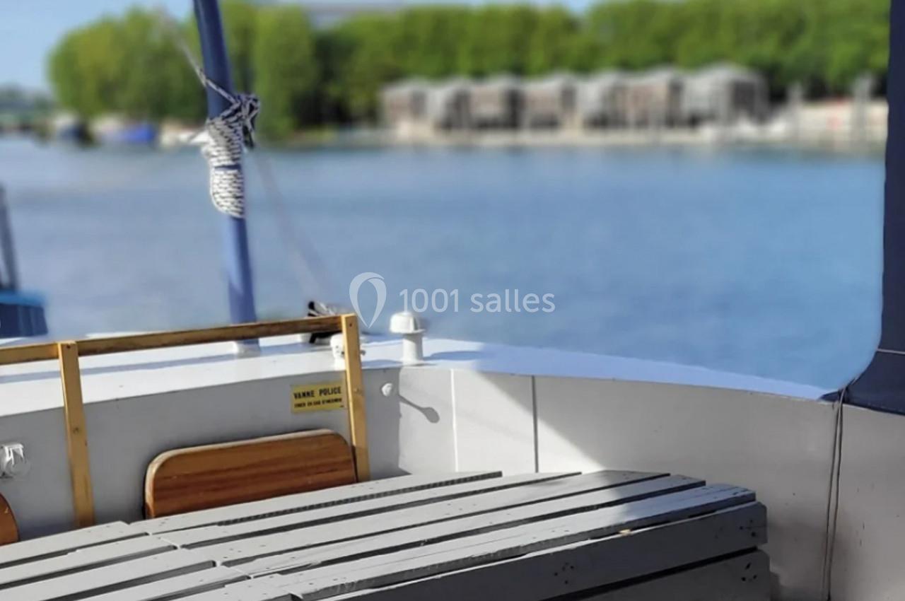 Vue depuis l'arrière d'un bateau avec des bancs en bois, une corde nouée et un paysage fluvial en arrière-plan.