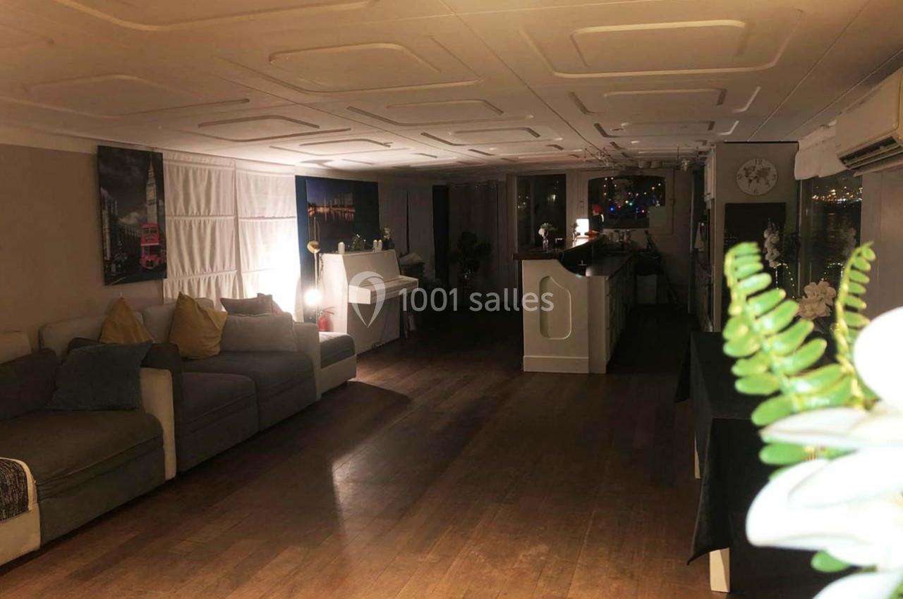 Intérieur d'une pièce lumineuse avec canapé, piano, bar et parquet, décorée de plantes et éclairée par des lumières tamisées.