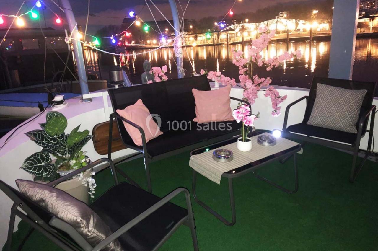 Espace extérieur aménagé sur un bateau avec des fauteuils, une table basse, des plantes et des guirlandes lumineuses…