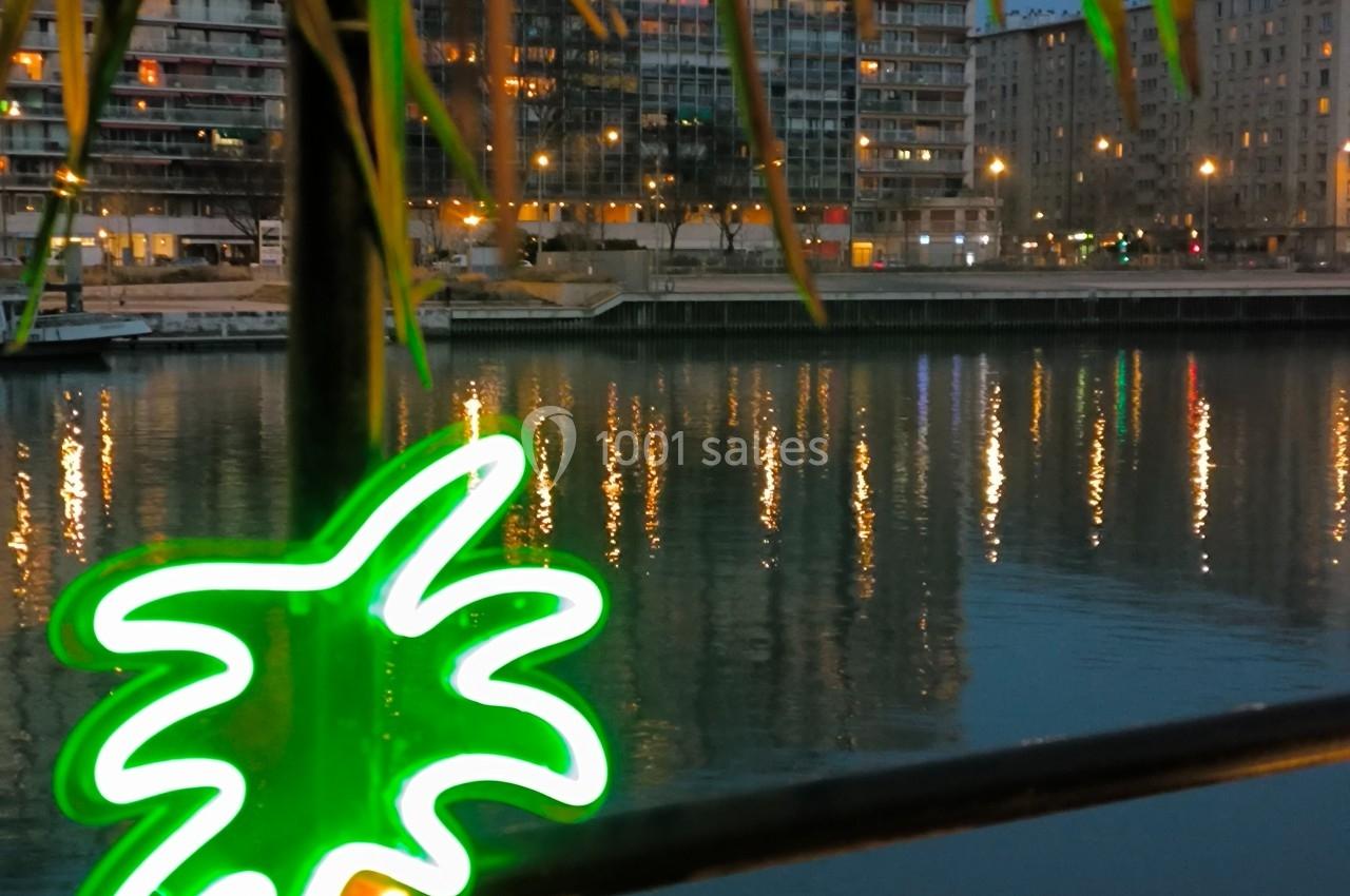 Vue nocturne d'un canal bordé d'immeubles illuminés, avec un néon en forme de palmier au premier plan.