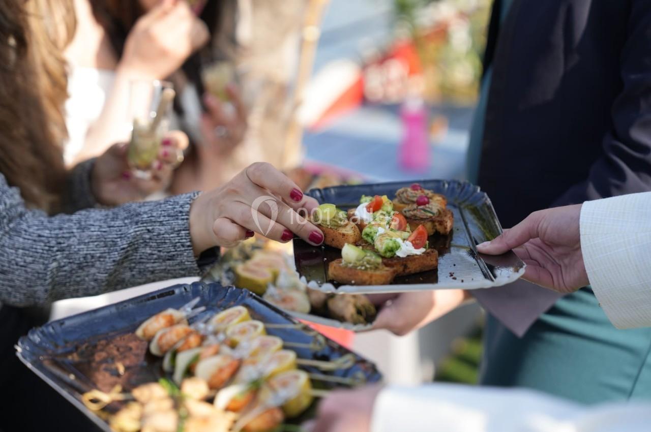 Des mains prennent des amuse-bouches variés sur des plateaux lors d'un événement en extérieur.
