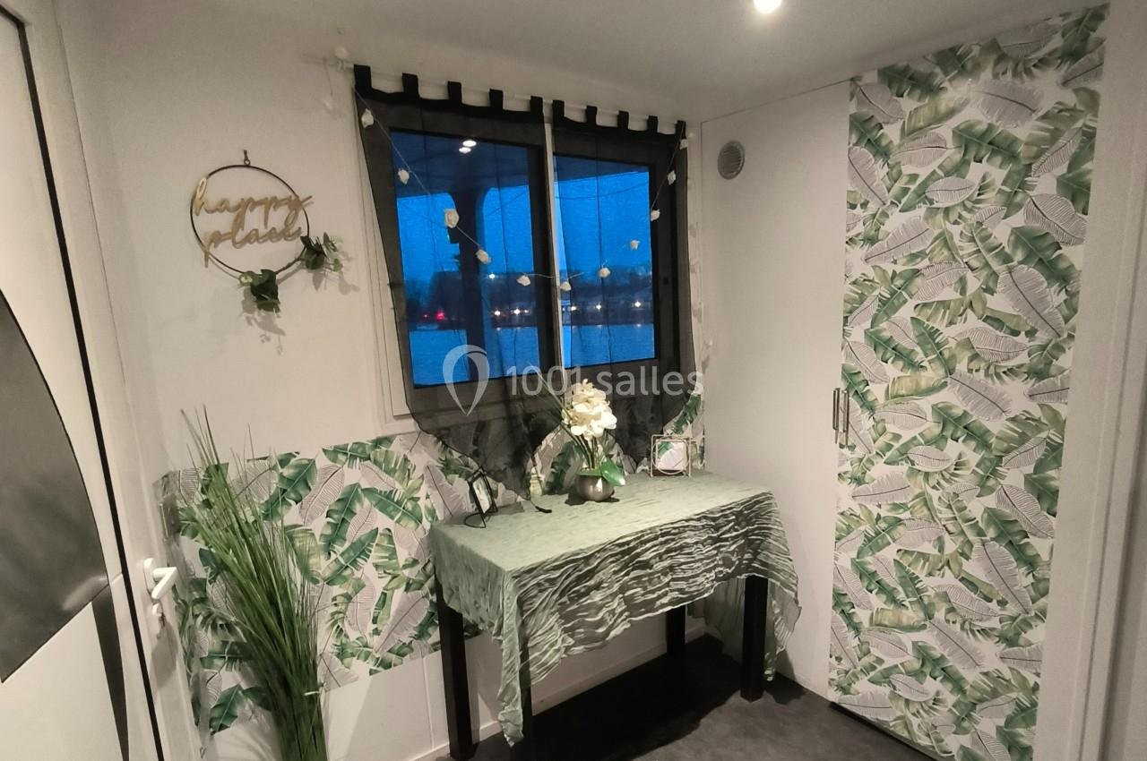 Décoration intérieure avec table recouverte d'un tissu vert, plantes, et murs ornés de motifs de feuilles tropicales.