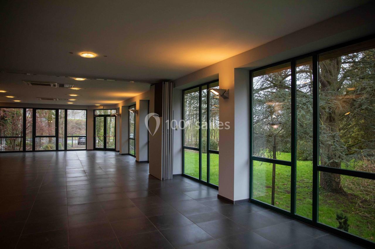 Salle vide avec de grandes baies vitrées donnant sur un espace extérieur verdoyant.