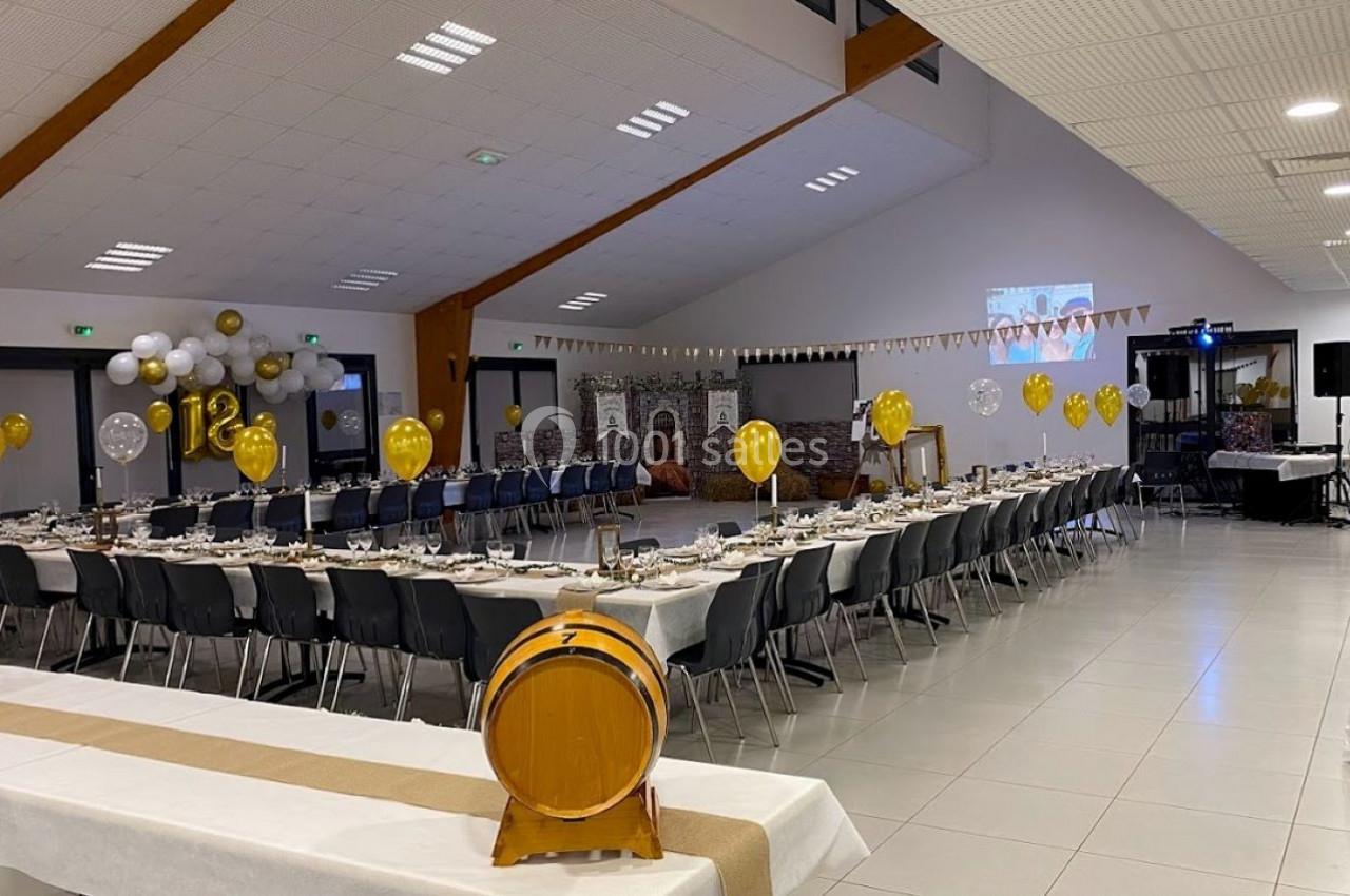 Salle de réception décorée avec des ballons dorés, tables dressées pour un événement et un tonneau en premier plan.