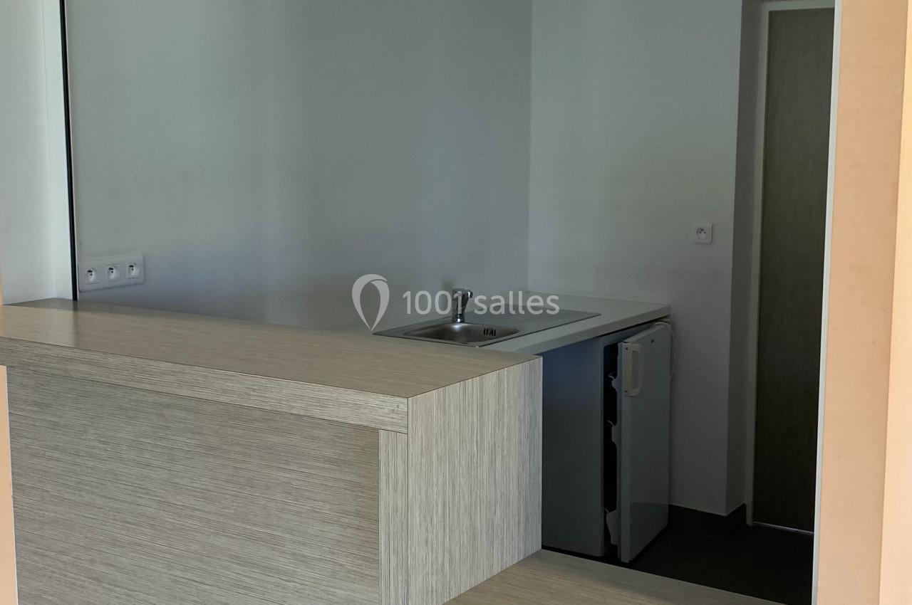 Comptoir en bois clair avec un évier intégré, situé dans un espace intérieur aux murs blancs et plafond à dalles.