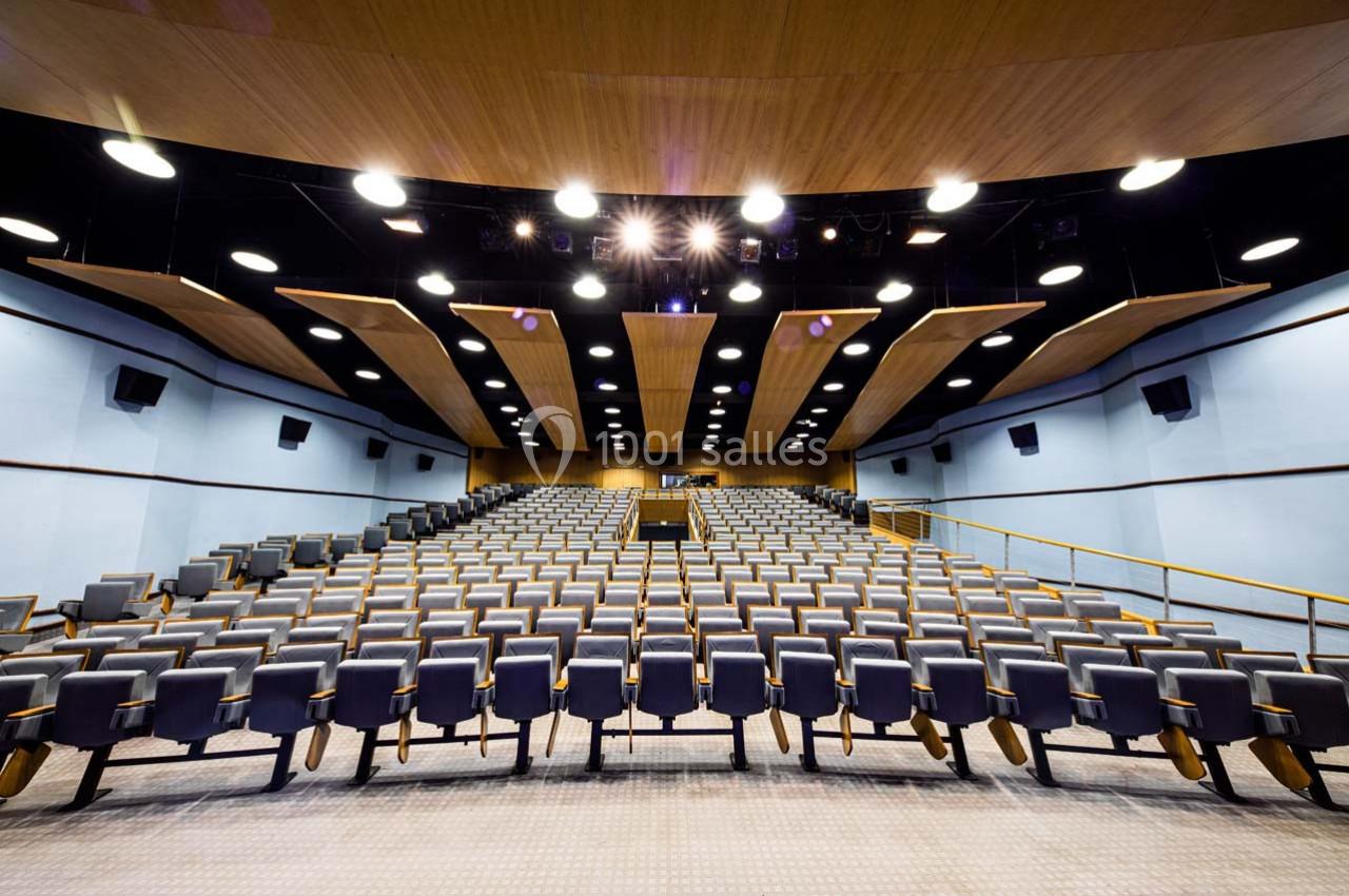 Salle de conférence moderne avec des rangées de sièges vides et un éclairage au plafond.