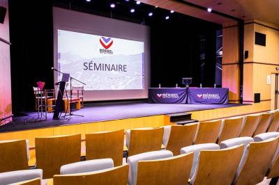 Entrée lumineuse avec tapis foncé, murs blancs, escalier en bois et plantes visibles à travers une cloison vitrée.