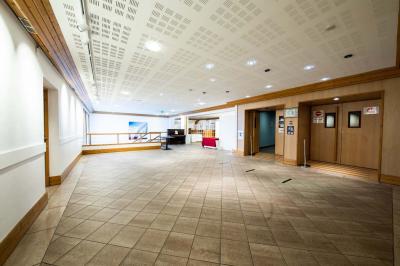 Entrée lumineuse avec tapis foncé, murs blancs, escalier en bois et plantes visibles à travers une cloison vitrée.