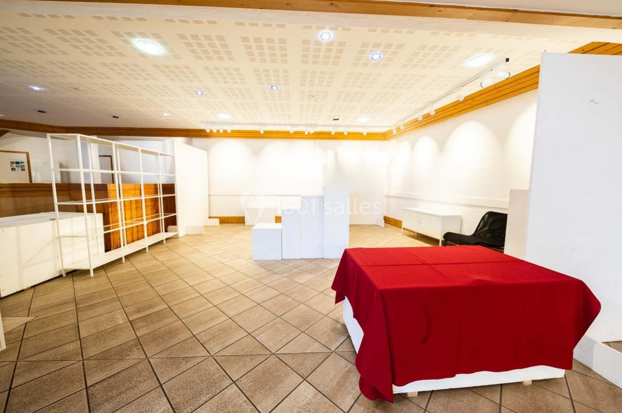 Salle vide avec carrelage au sol, murs blancs, étagères ouvertes et une table recouverte d'une nappe rouge.