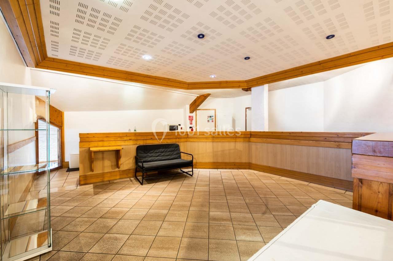 Hall d'entrée avec comptoir en bois, canapé noir, présentoir en verre et carrelage beige.