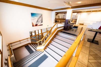 Entrée lumineuse avec tapis foncé, murs blancs, escalier en bois et plantes visibles à travers une cloison vitrée.