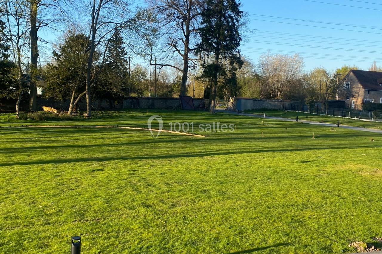 Pelouse verte avec quelques arbres en arrière-plan, entourée de clôtures et éclairée par une lumière naturelle.